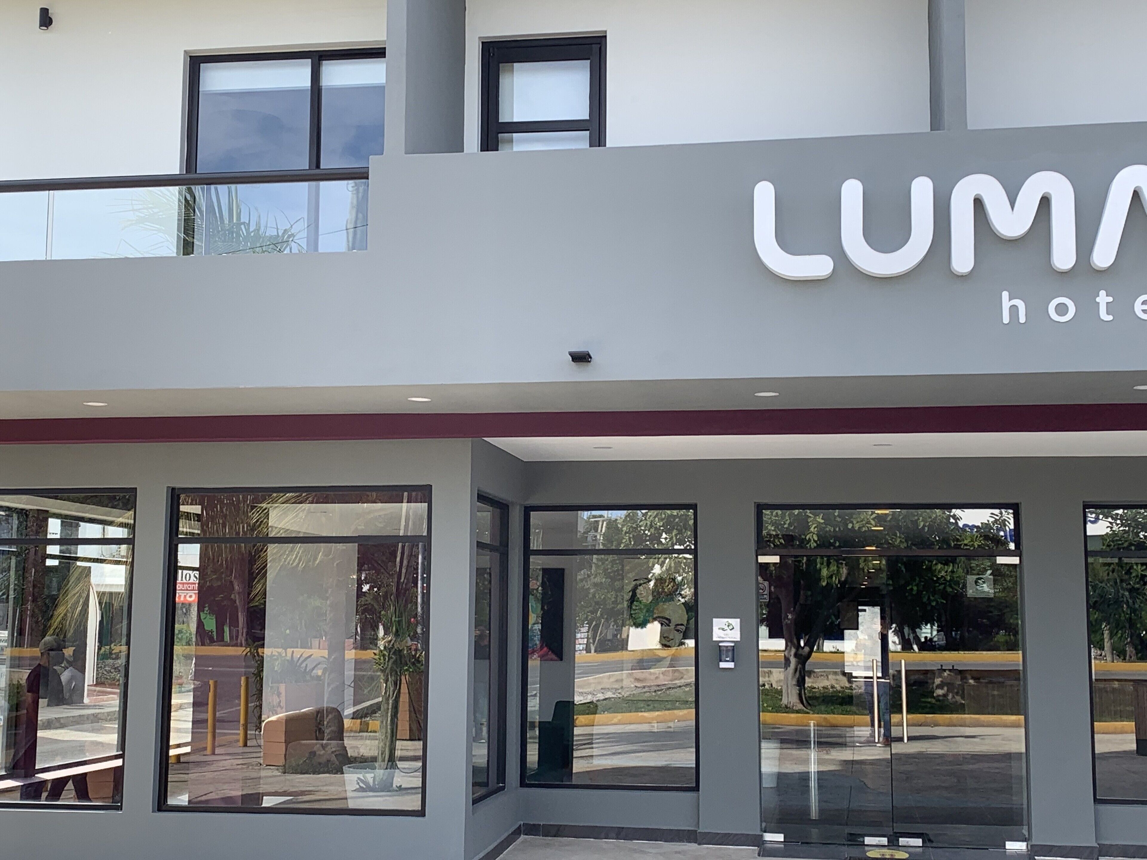 Ein moderner Hotel Eingang mit Glasfassade, großen Fenstern und einem sichtbaren Schild mit der Aufschrift "LUMA hotel".