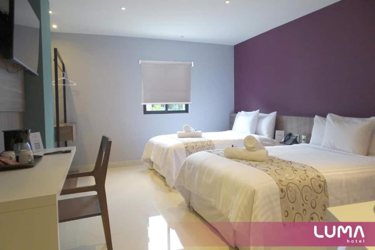 Une chambre d’hôtel avec deux lits, un bureau et une fenêtre avec des stores.