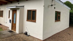 A single-story building with a white exterior, a wooden door, and two windows with wooden frames. - 1-bedroom Ground Floor Near Rugby School (Rugby)