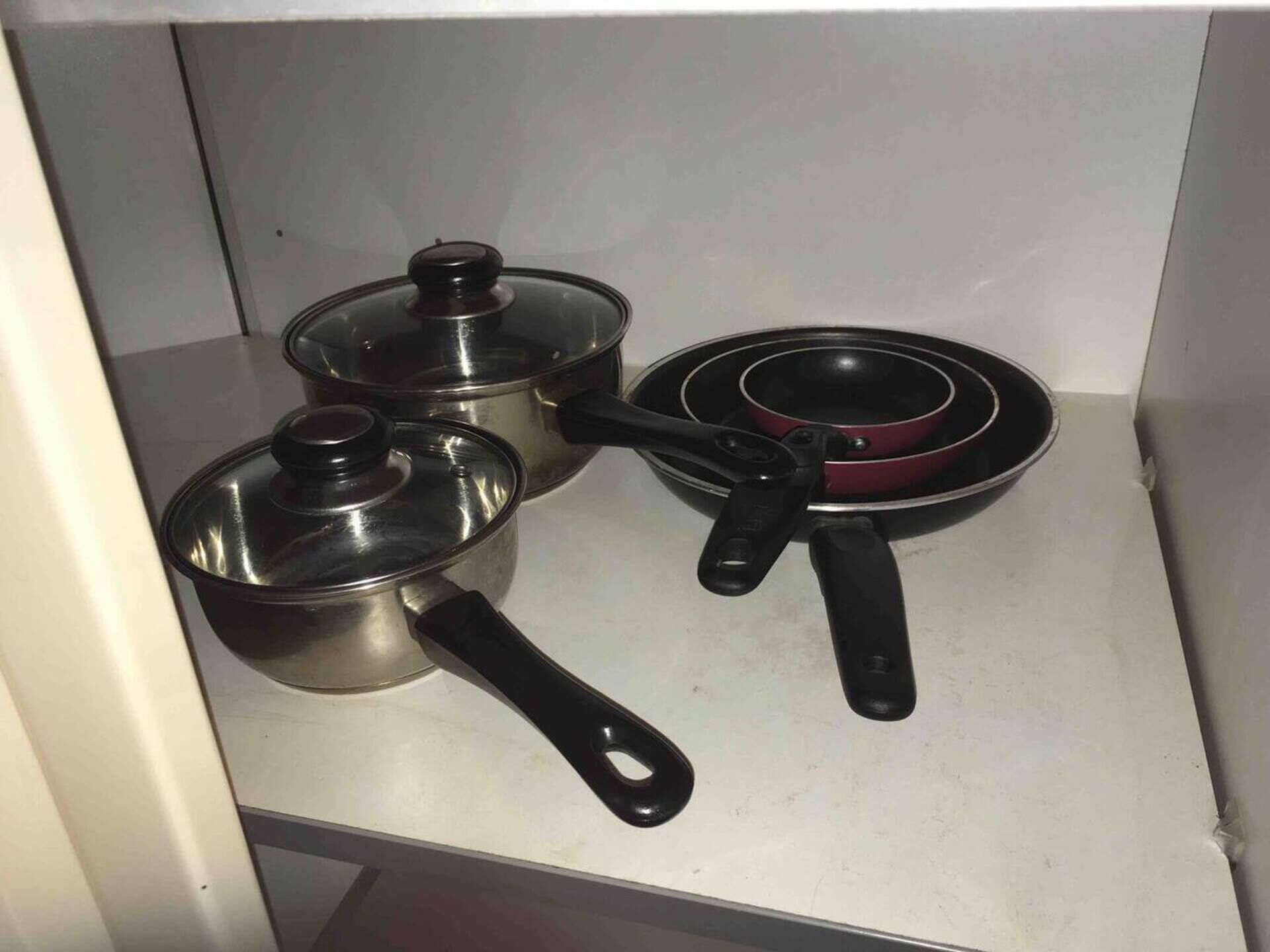 Een keuken met roestvrijstalen pannen en een koekenpan op een wit aanrecht.