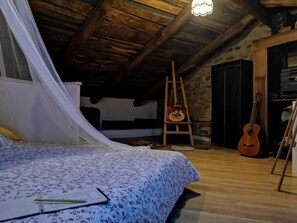Una habitación rústica con techo de madera, una cama con colcha floral, una guitarra y un caballete.