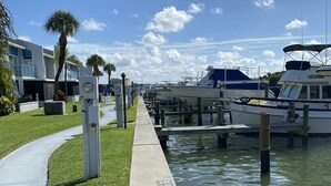 A marina with boats docked, a concrete walkway, and a building with balconies.