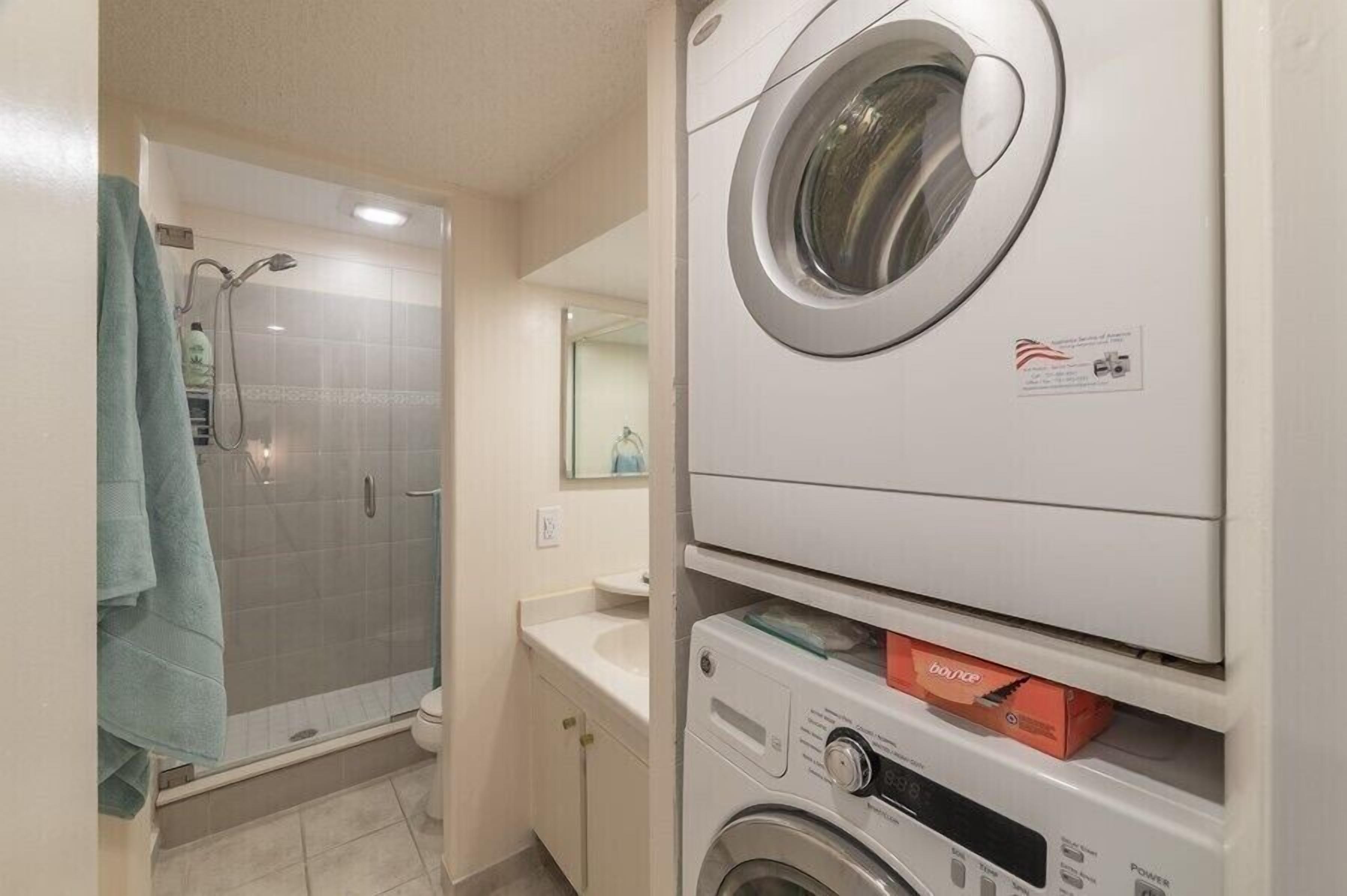 A compact bathroom with a shower, a washing machine, and a sink.