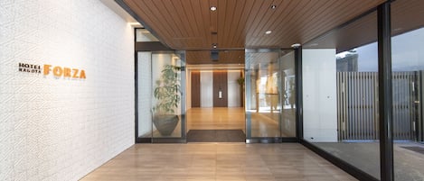 Un moderno hall de hotel con techo de madera, puertas de vidrio y un cartel que dice 'Hotel Nagoya Forza'.