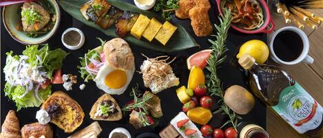 Diversos alimentos, incluindo sanduíches, pão e frutas, dispostos sobre uma mesa preta.