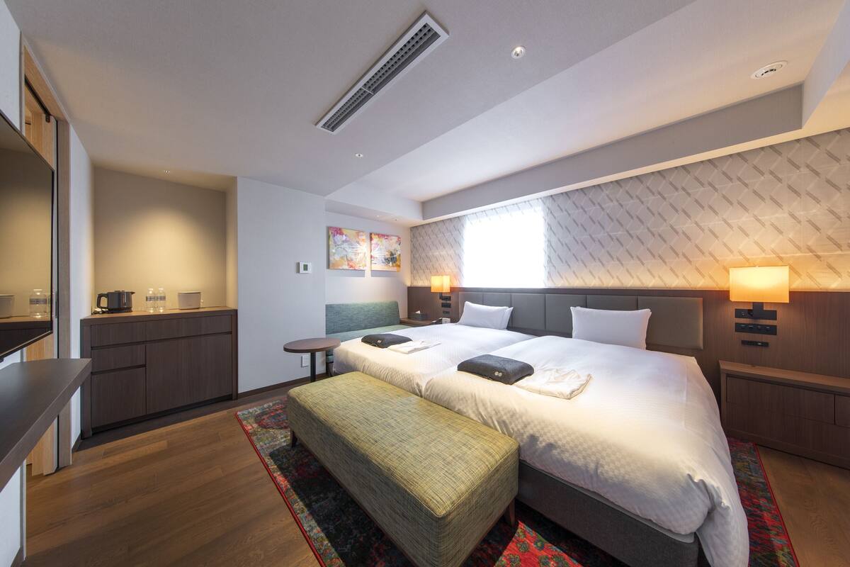 A modern hotel room with a large bed, a desk, a chair, and a small table.