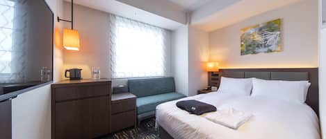 A hotel room with a bed, a desk, a chair, a window with curtains, a painting on the wall, and a lamp.