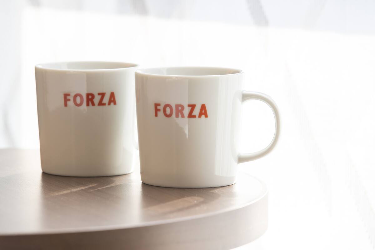 Two white ceramic mugs with the word "FORZA" printed on them, placed on a round wooden table.
