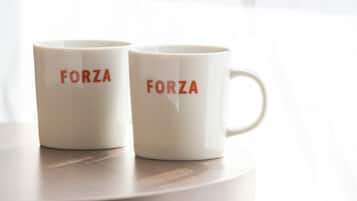 Two white ceramic mugs with the word "FORZA" printed on them, placed on a round wooden table.