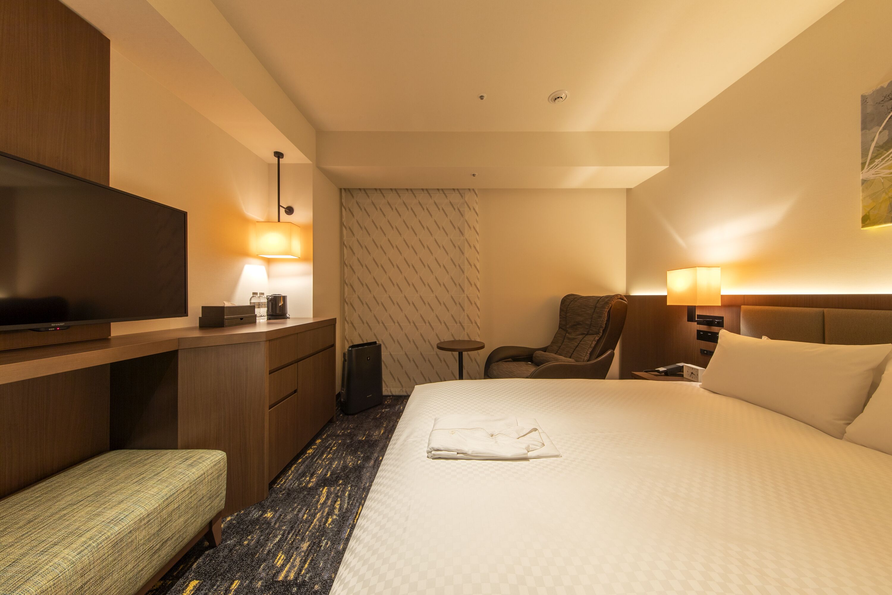 A hotel room with a bed, a desk, a television, a chair, and a small table.