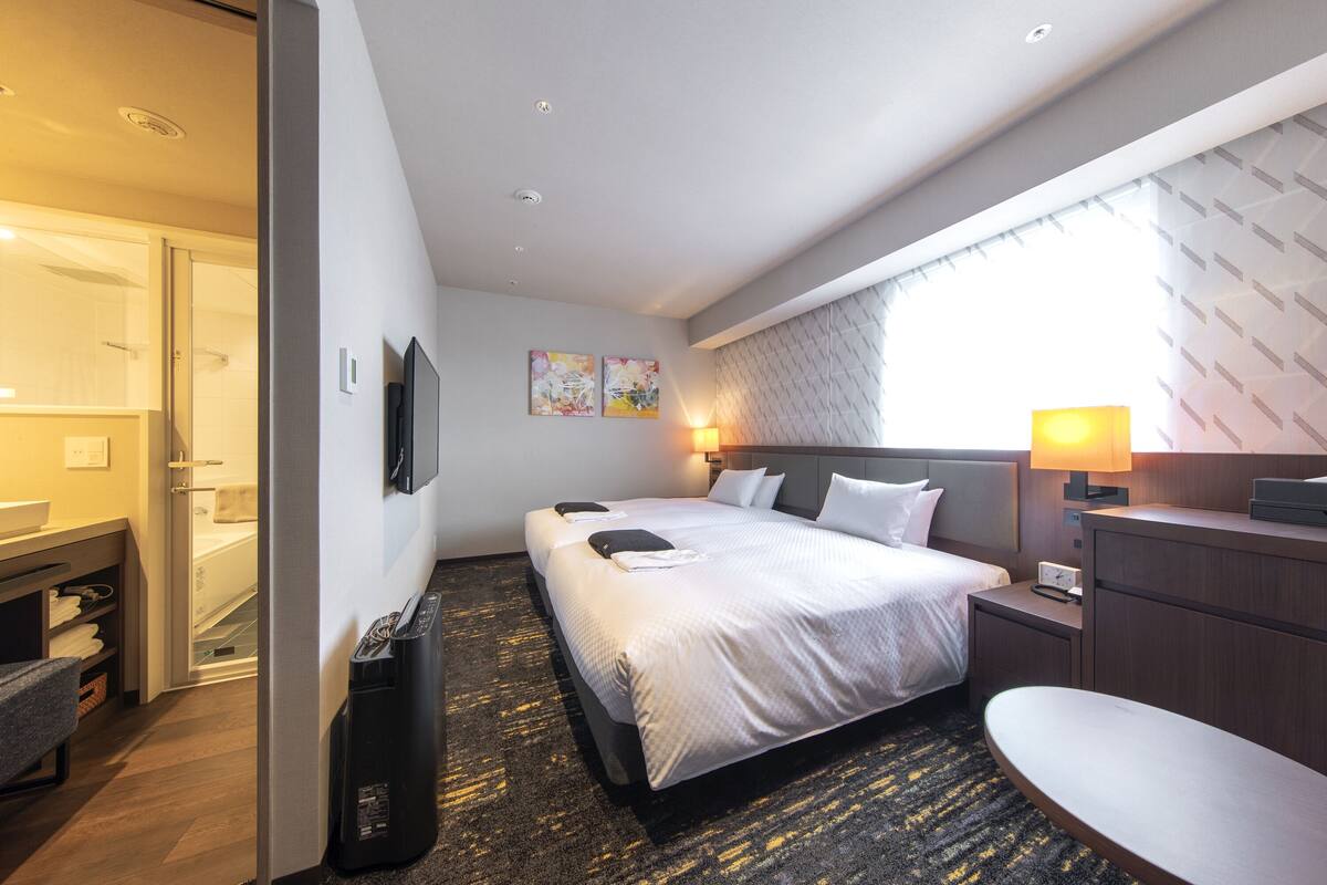 A modern hotel room with a large bed, a desk, a chair, and a TV.