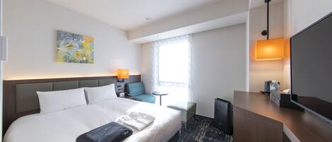 Een moderne hotelkamer met een groot bed, een bureau met een flatscreen televisie, een klein tafeltje en een stoel.