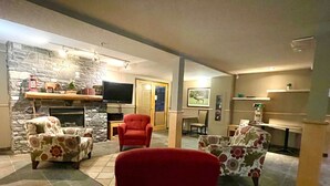 Ein Wohnzimmer mit Kamin aus Stein, einem Fernseher und zwei Sesseln.