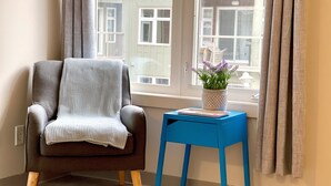 Ein Zimmer mit einem braunen Sessel, einem blauen Beistelltisch und einem Fenster mit Vorhängen.