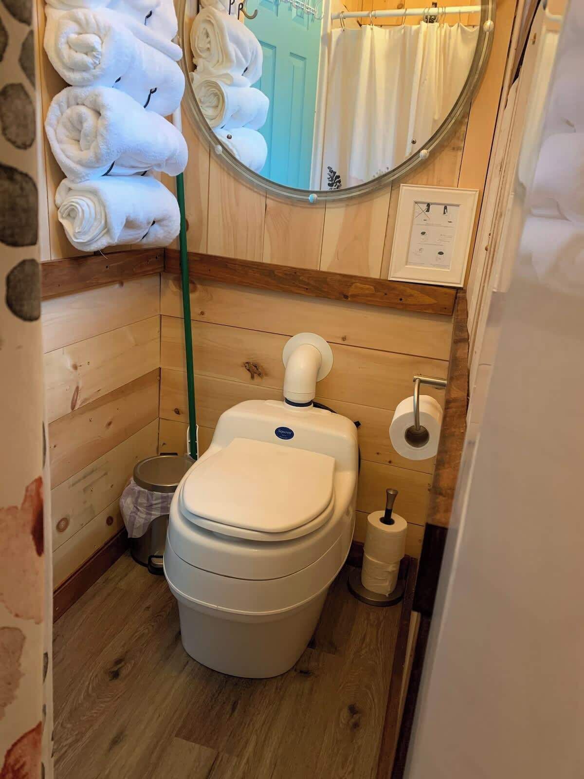 Et lille badeværelse med toilet, en skraldespand og et håndklædestativ med sammenfoldede håndklæder.