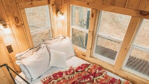 A wooden cabin bedroom with a bed, windows, and a staircase.