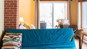 Een gezellige kamer met een blauwe bank, een houten tafel met kop en schotel, en een wastafel.