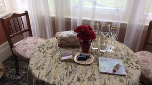A round table with a floral tablecloth, a vase of red roses, a plate with a chocolate bar, and a coloring book. - Relax in style at the Catlins Retreat, historic villa in the heart of Owaka (Owaka)