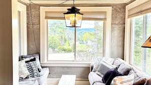 A cozy living room with a wooden ceiling, a hanging lantern, a sofa set, and a view of greenery outside.