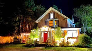 A two-story wooden house with a red door, a front porch, and a small attached garage.