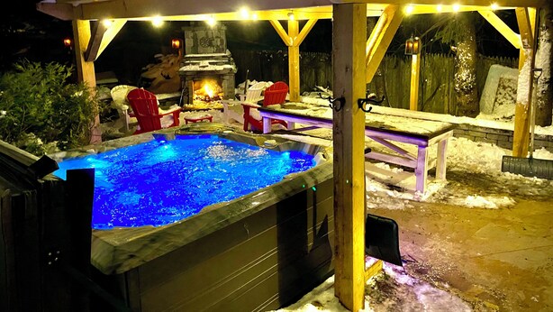 A hot tub with a wooden pergola overhead, surrounded by snow.
