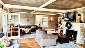 A spacious living room with a fireplace, wooden ceiling, and a large TV mounted above it.