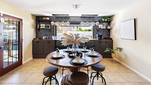 Una cocina moderna con armarios oscuros, una mesa redonda de comedor con seis sillas y lámparas colgantes.