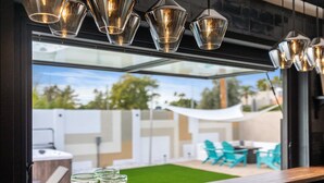 Un área de estar exterior moderna con una pared de cristal, una parrilla para barbacoa y vistas al jardín.