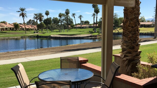 Eine Terrasse mit rundem Tisch und Stühlen, mit Blick auf einen Golfplatz und ein Gewässer.