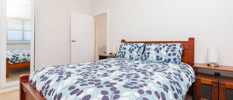 Quarto com cama de madeira, mesa de cabeceira, espelho e porta.