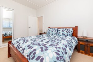 A bedroom with a wooden bed, a nightstand, a mirror, and a door. - Douglas 5 (Forster)