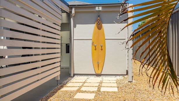 A building with a surfboard-shaped door, a gated entrance, and a palm tree in the foreground. - Douglas 5 (Forster)