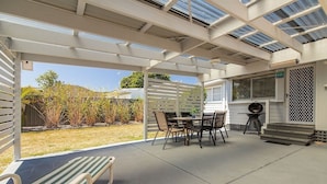 A covered patio area with a table and chairs, a lounge chair, and a view of the backyard. - Douglas 5 (Forster)