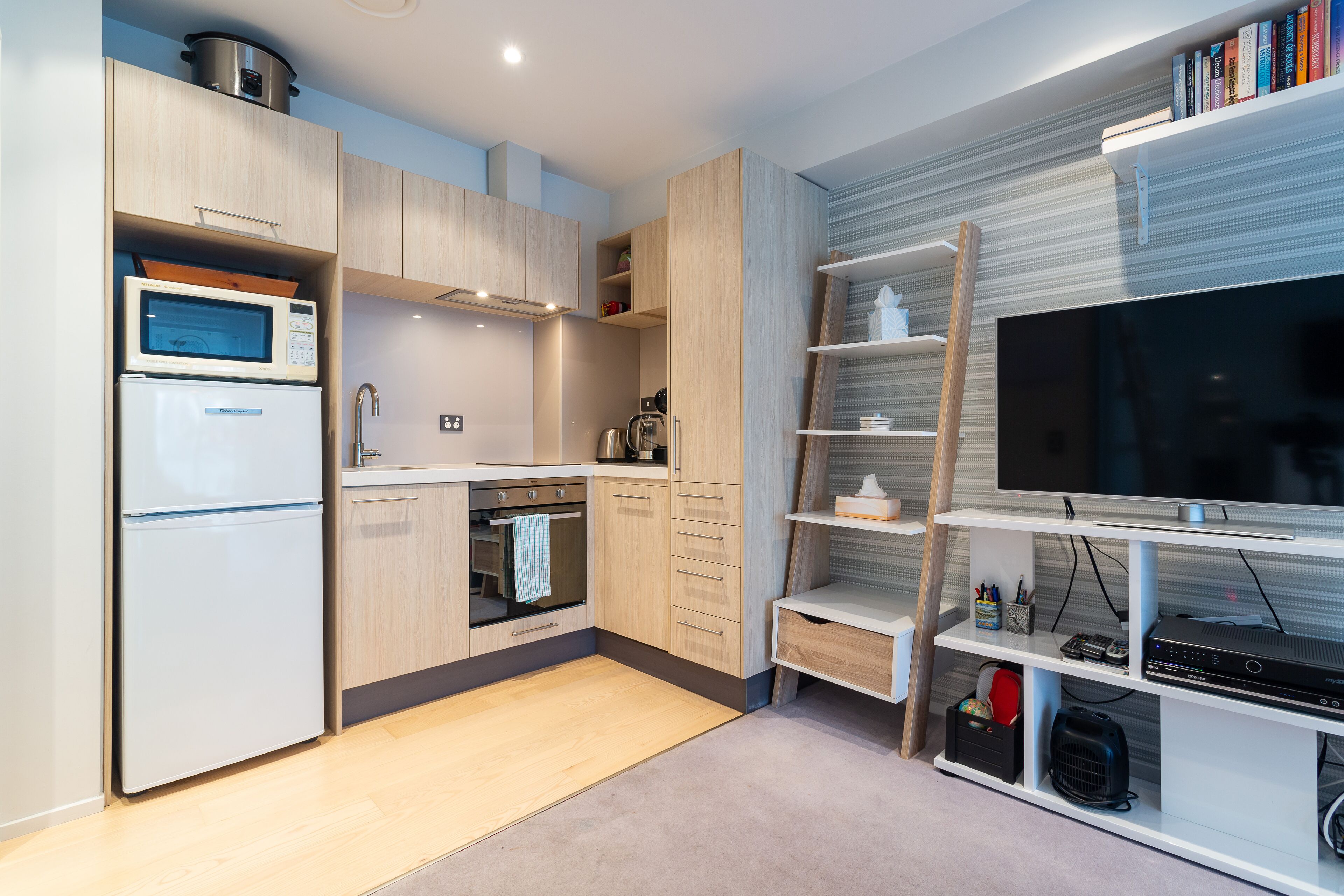 Una cucina compatta con elettrodomestici moderni, forno integrato e televisore su un ripiano.