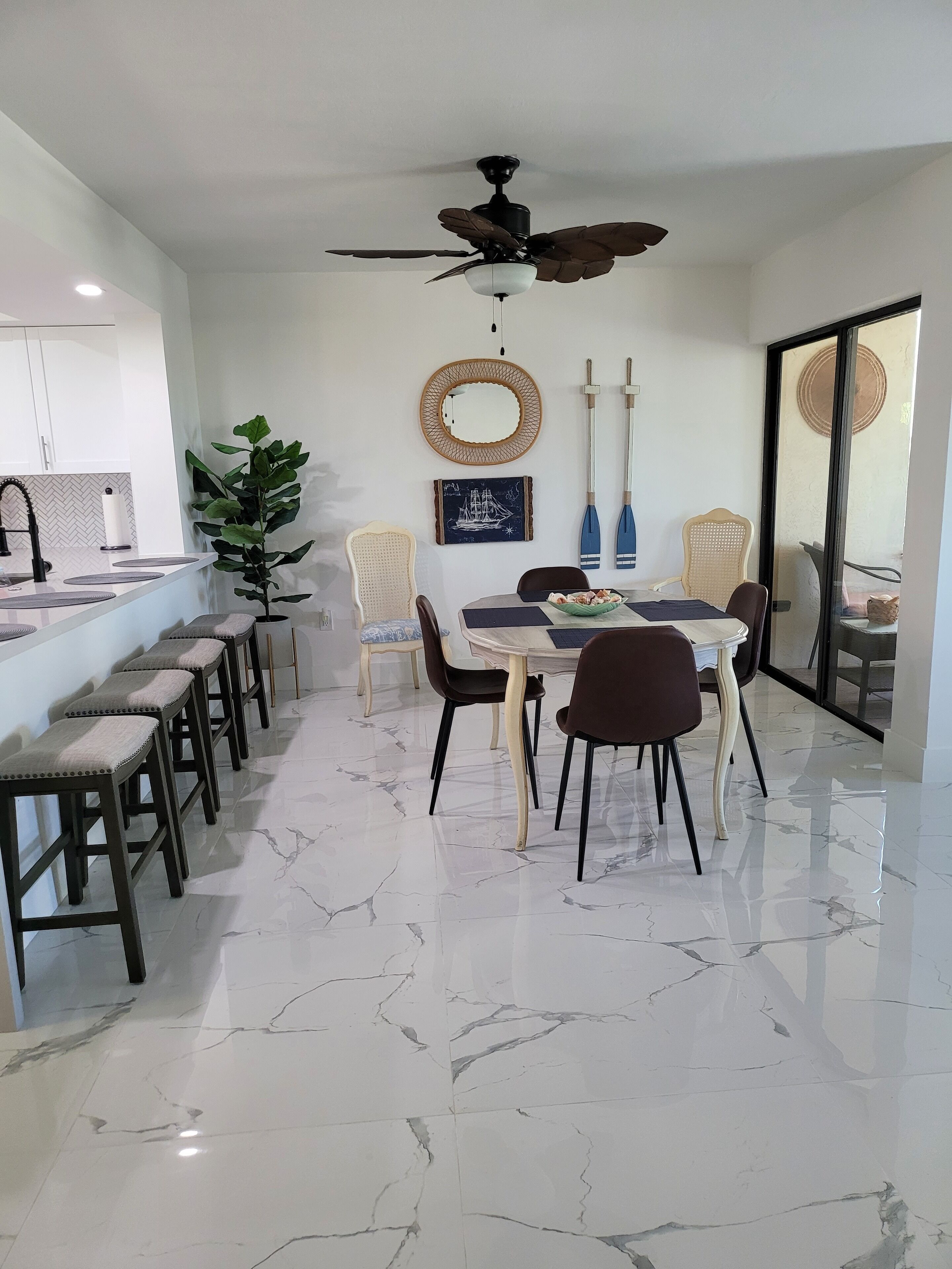 A dining area with a marble floor, a ceiling fan, a round mirror, and a table set with chairs.