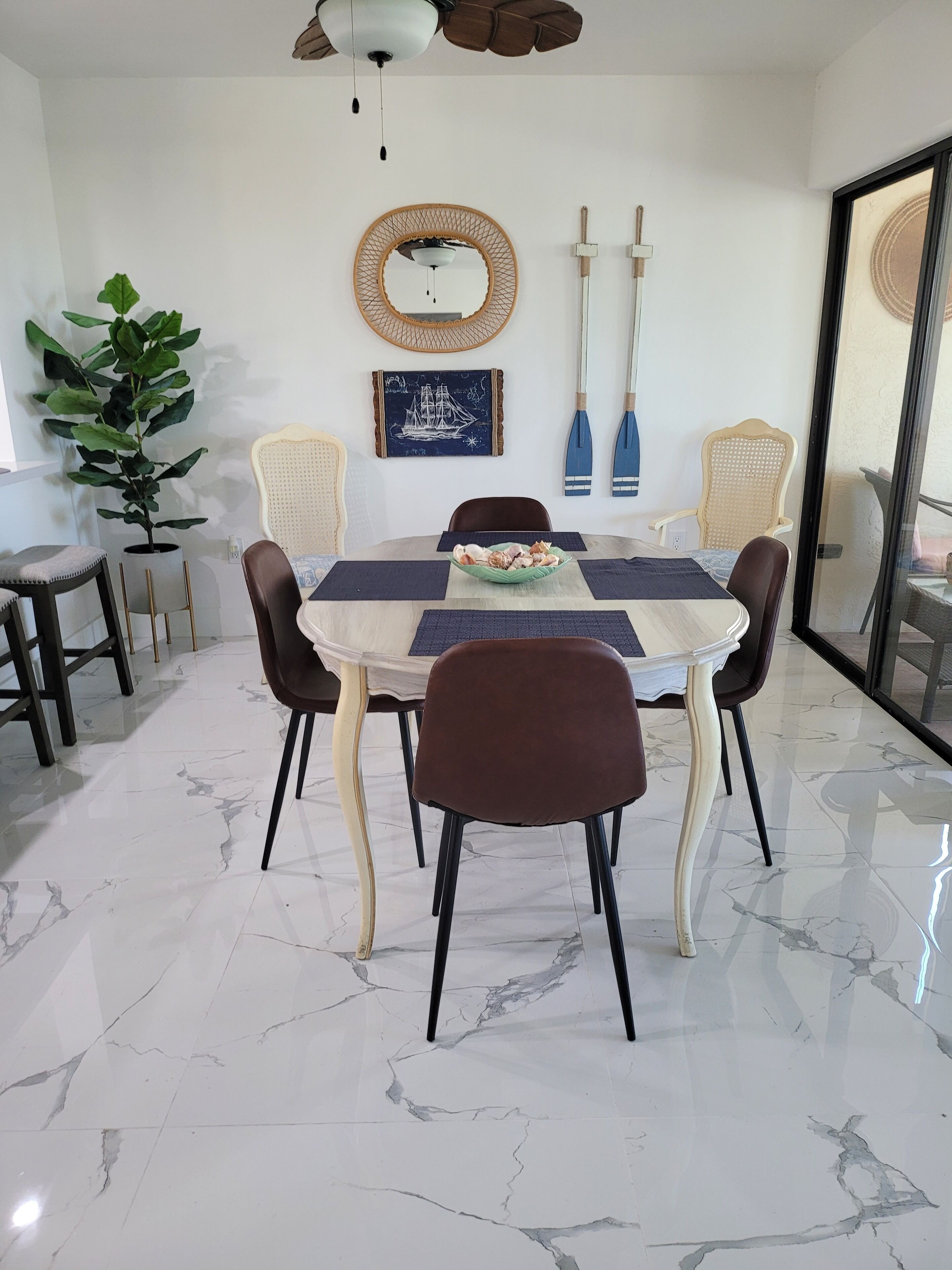 A dining area with a marble floor, a round table with six chairs, a potted plant, and a wall-mounted mirror.