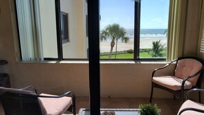 A room with a view of the beach, two chairs, a table, and a potted plant. - Coastal Escape ● Steps to Beach ● Sunset Views (Fort Myers Beach)