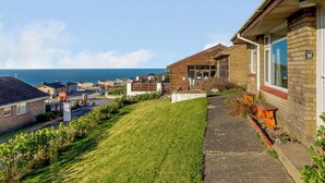 Un barrio residencial con casas, una pendiente cubierta de césped y vista al mar.
