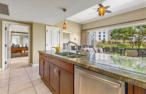 A modern kitchen with a granite countertop, stainless steel appliances, and a view of the outdoor patio. - Maui Resort Rentals: Honua Kai Hokulani 144 – Large Ground Floor 1BR, Spacious Lawn Area + Easy Pools/Beach Access (Lahaina)