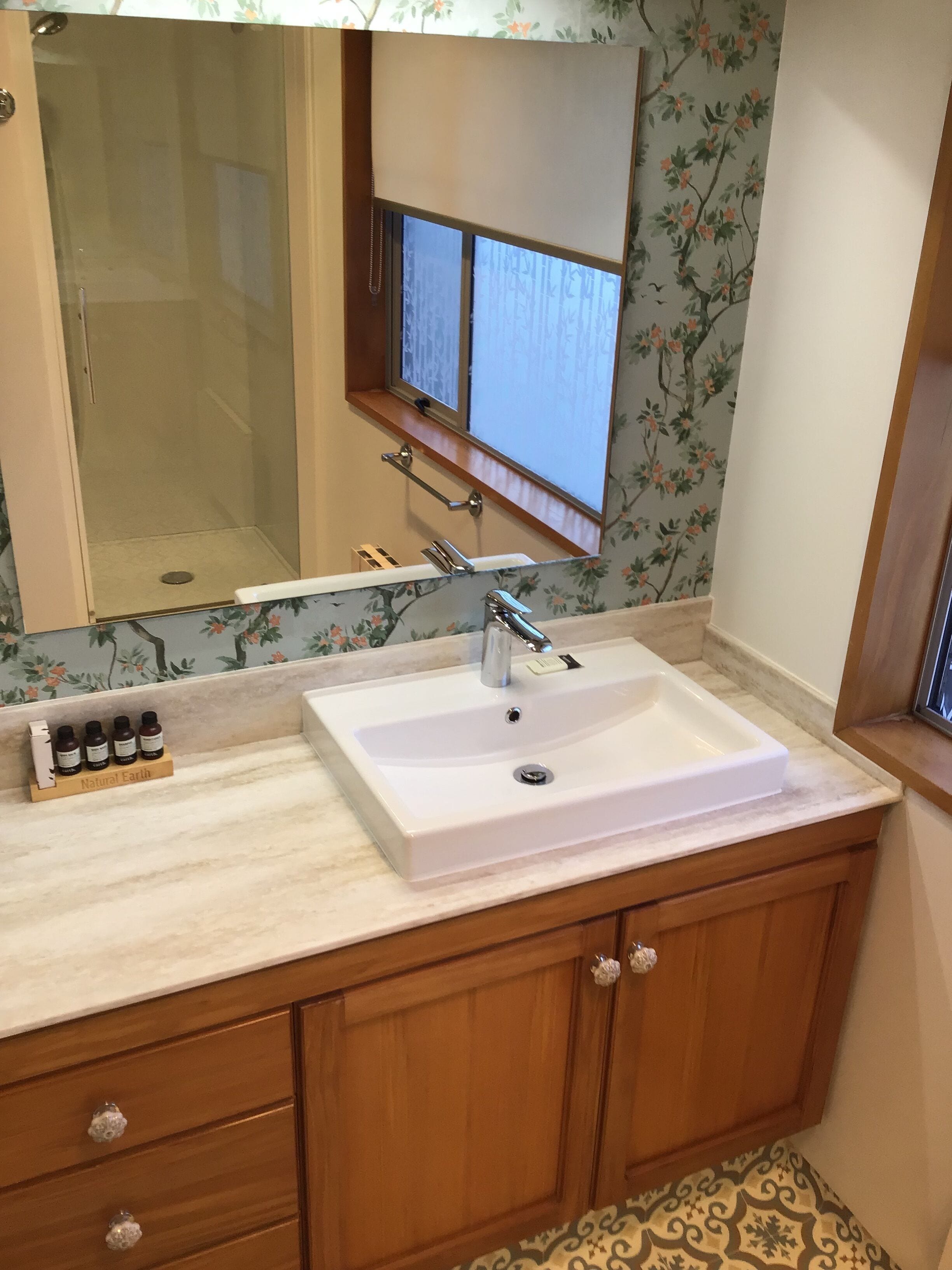 A bathroom with a white sink, wooden cabinets, a mirror, and a window with a view.