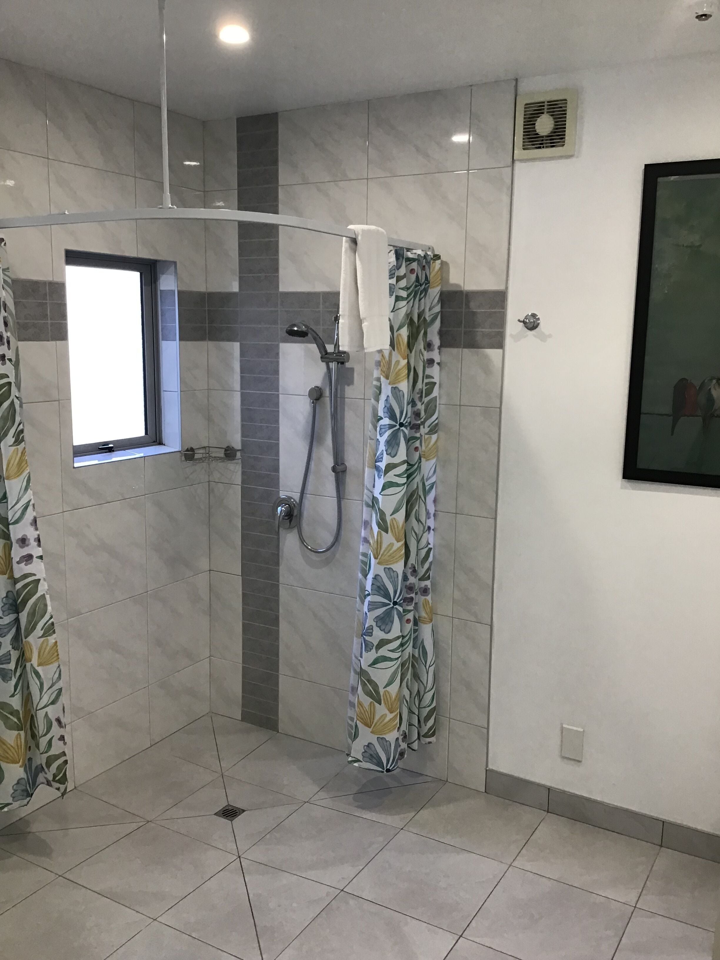 A bathroom with a shower, a window, and a tiled floor.