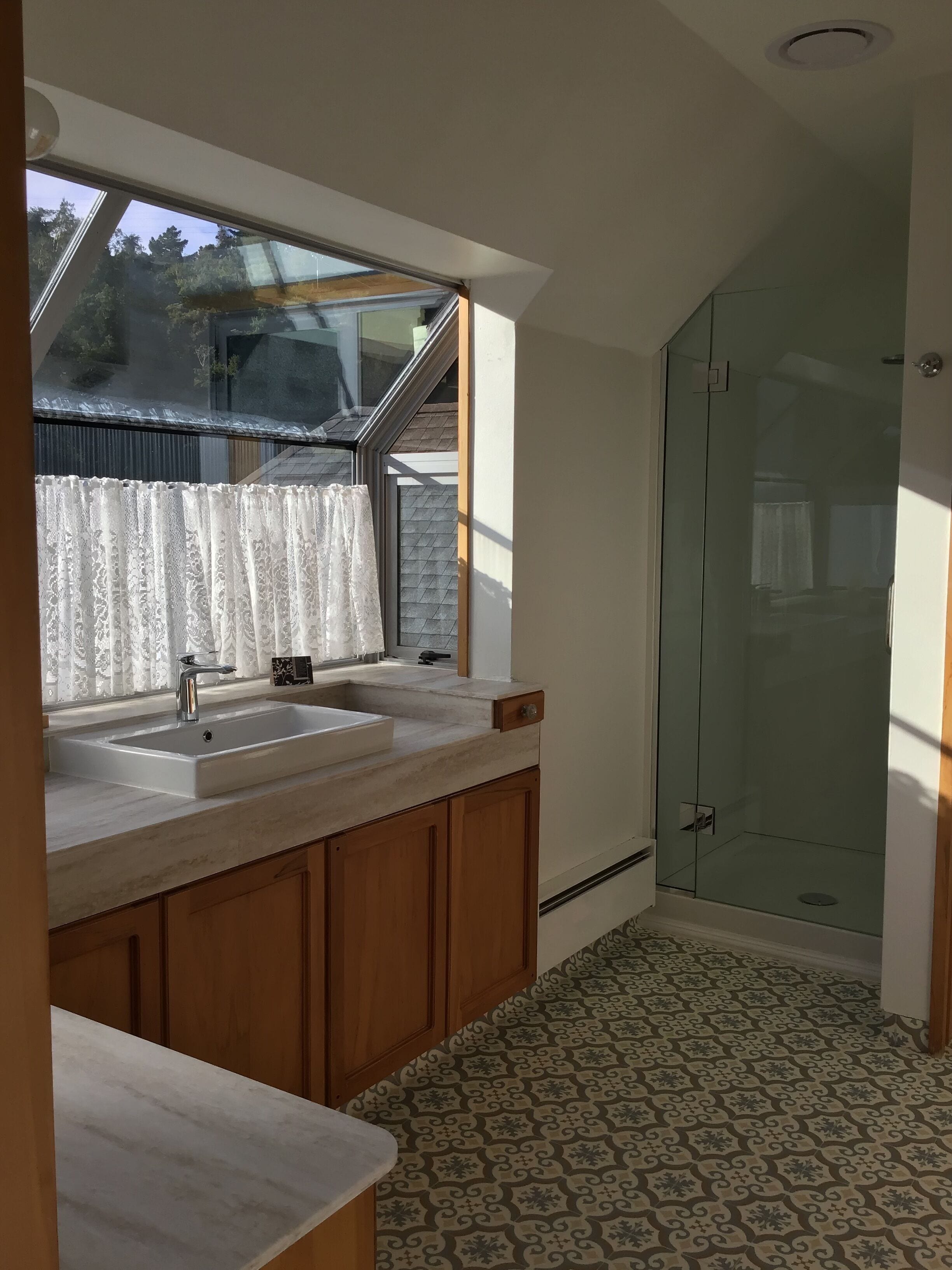 A bathroom with a shower, a sink with a window, and patterned floor tiles.
