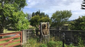 A garden with a wooden fence, a stone bear sculpture, and various plants. - Woodland Glen Lodge (Hokitika)