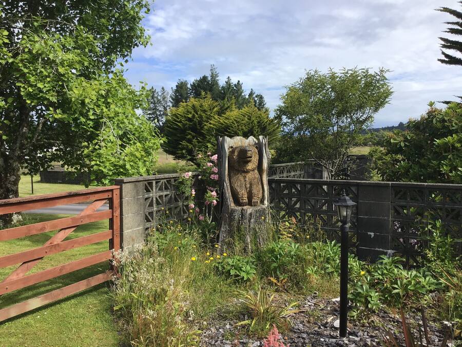 A garden with a wooden fence, a stone bear sculpture, and various plants.