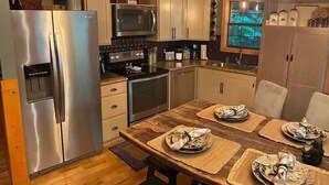 A modern kitchen with stainless steel appliances, wooden flooring, and a dining table set for four. - Rally Point, Creekside retreat in the Smokies` (Sevierville)