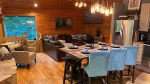 A cozy cabin interior with a wooden dining table set for four, a sofa, and a kitchen area with a refrigerator and stove. - Rally Point, Creekside retreat in the Smokies` (Sevierville)