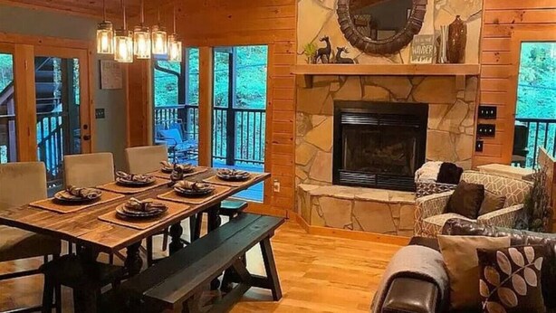 A cozy cabin interior with a stone fireplace, wooden dining table, and comfortable seating. - Rally Point, Creekside retreat in the Smokies` (Sevierville)