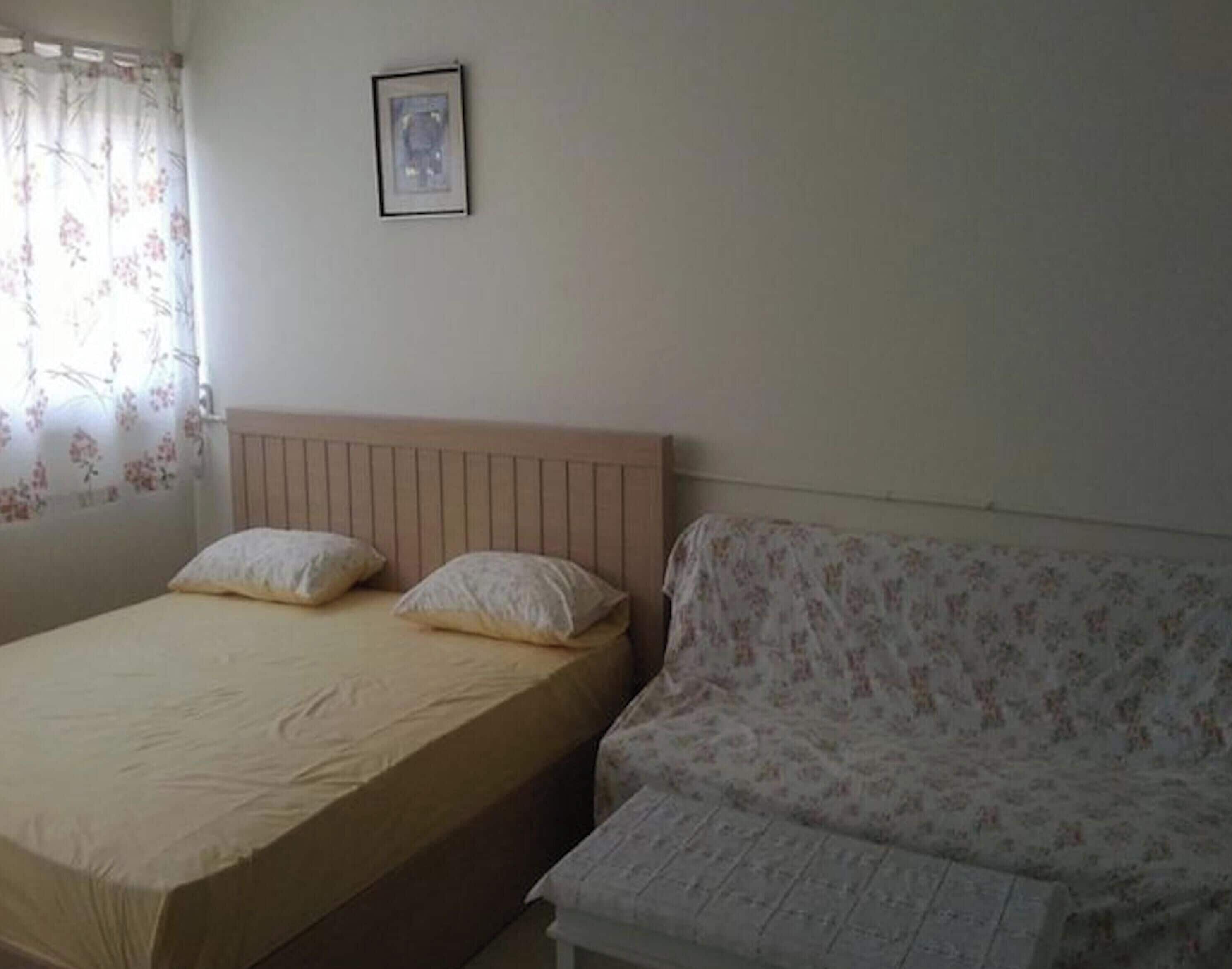 A bedroom with a bed, a sofa, a framed picture on the wall, and a window with floral curtains.