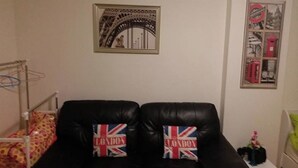 A room with two black leather chairs, a bed with a polka dot blanket, a framed picture of the Eiffel Tower, and a framed picture of a red telephone booth. - Room-poppular Palace Don Mueang Bangkok (Pak Kret)