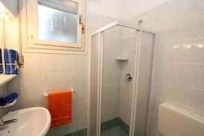 A bathroom with a white sink, an orange towel, a glass-enclosed shower, and a window with a frosted glass panel.